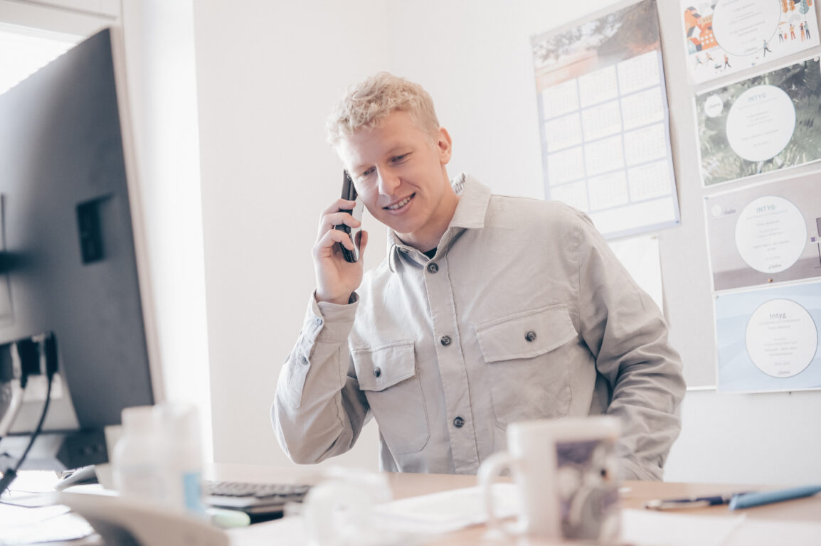 Person sitter vid ett skrivbord och pratar i telefonen.